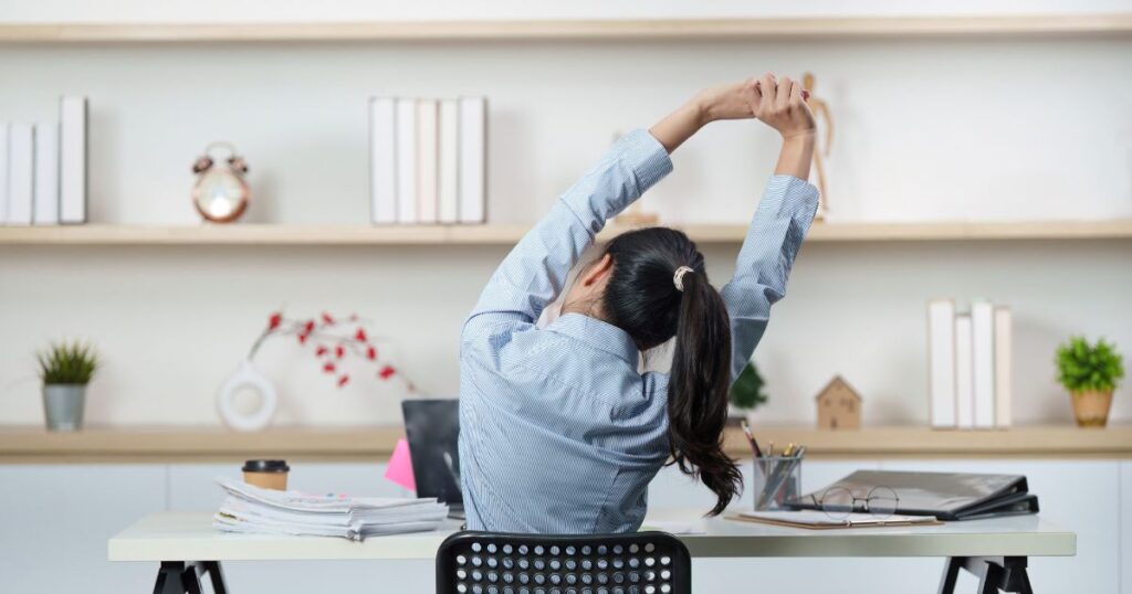 Person dehnt Schultern und Arme am Schreibtisch, um Verspannungen zu lösen und die Beweglichkeit im Arbeitsalltag zu fördern.